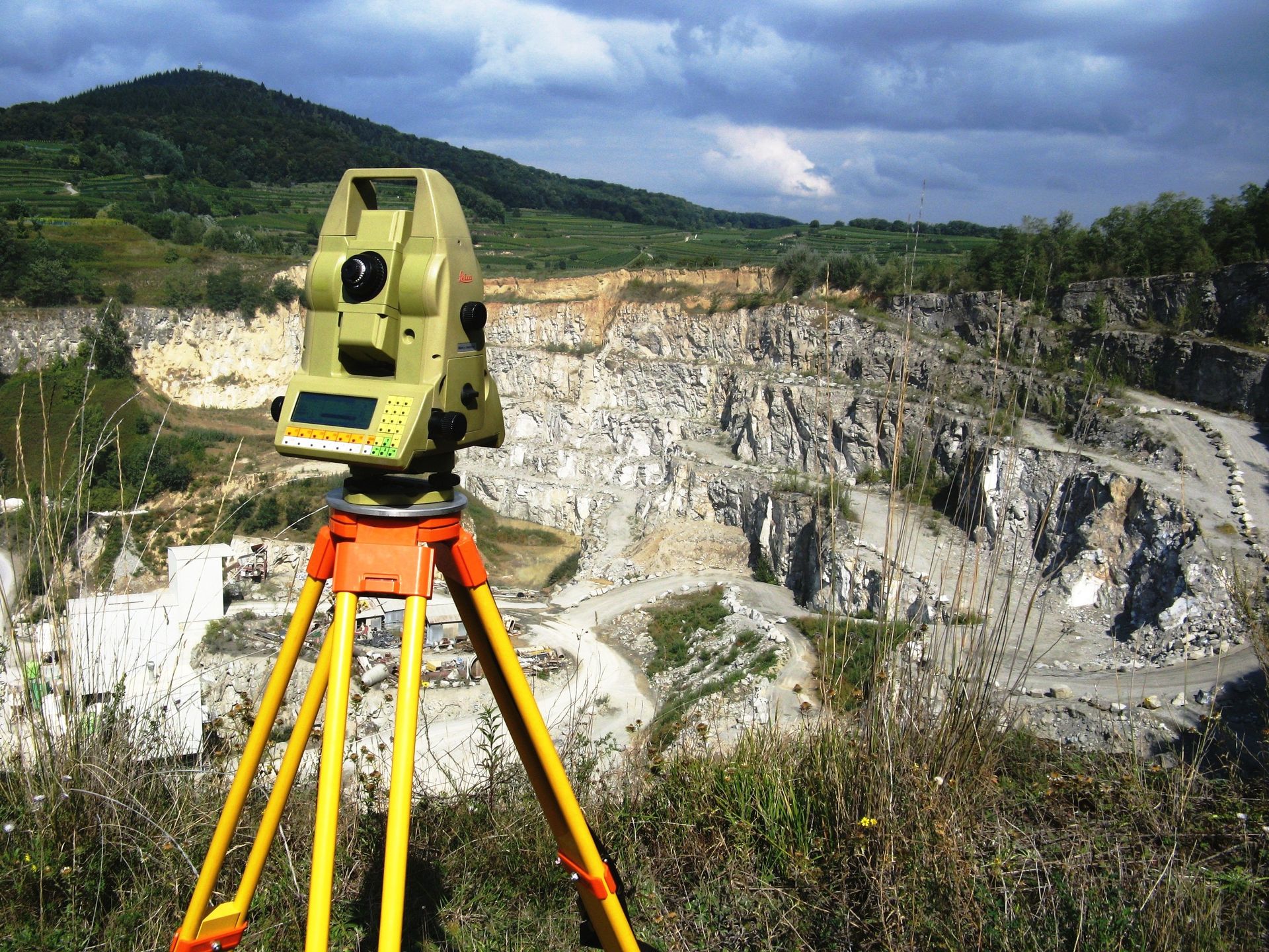 Vermessungsgeräte auf einem Stativ, positioniert mit Blick auf einen felsigen Steinbruch und einen Hügelhang im Hintergrund.
